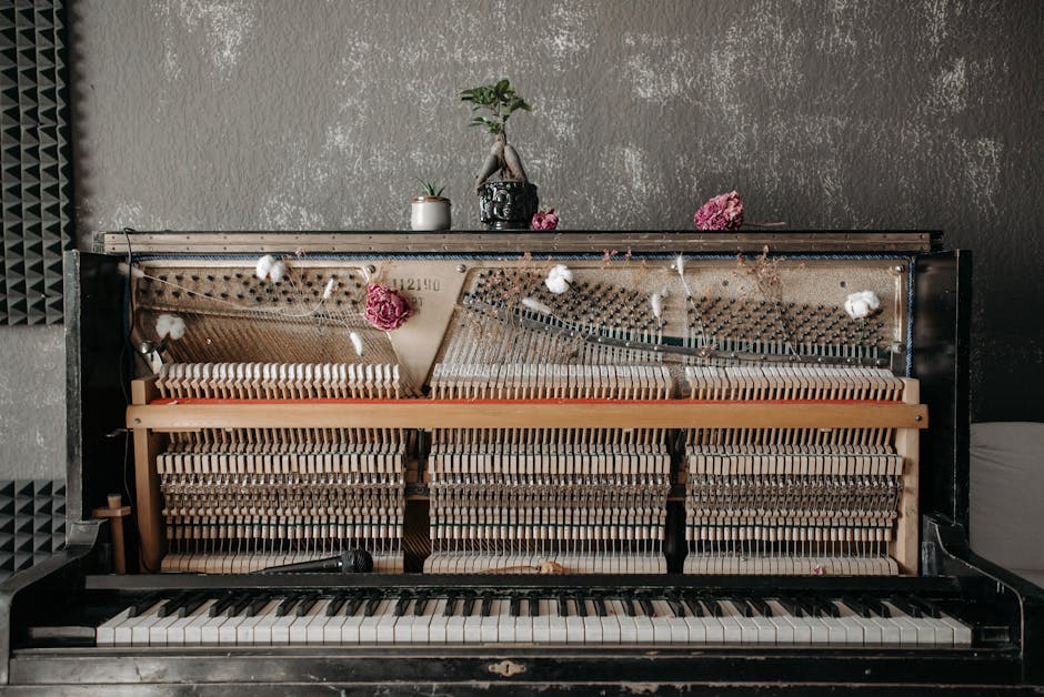 A vintage upright piano with exposed strings, adorned with flowers and a bonsai, in an acoustic studio setting.