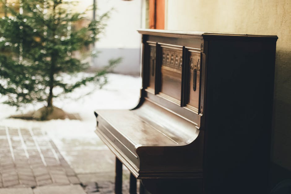 A classic wooden piano placed by a window overlooking a snowy tree.