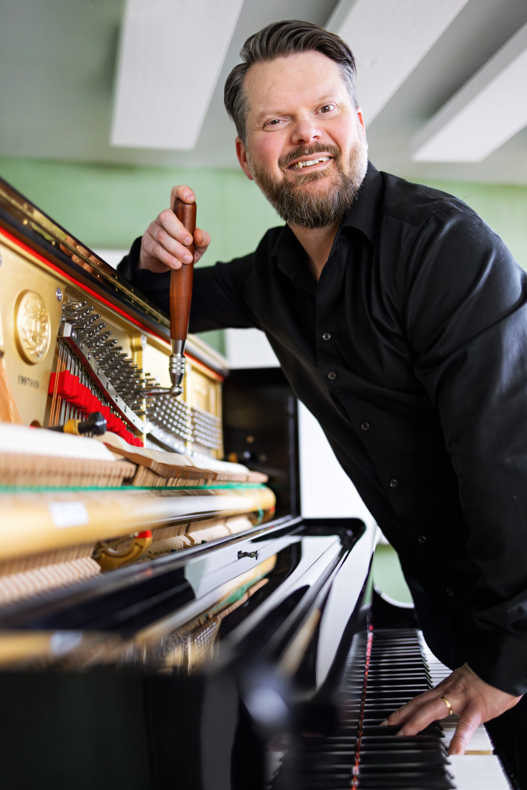 Tobias Granbacka stämmer ett öppet Kawai-piano med stämnyckel.